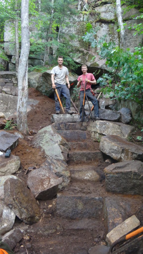 Two crewmembers stand atop a staircase still under construction. Champney Falls Trail
